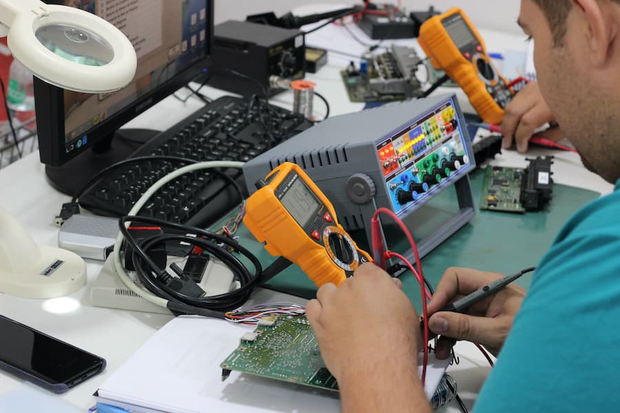 Student practicing ECU repair at a bench with a multimeter and test equipment